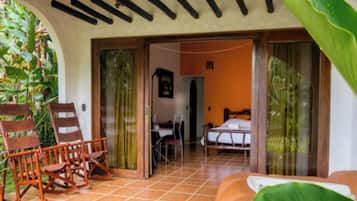 A room with a bed, a desk, and a rocking chair. There is a sliding door leading to another room.