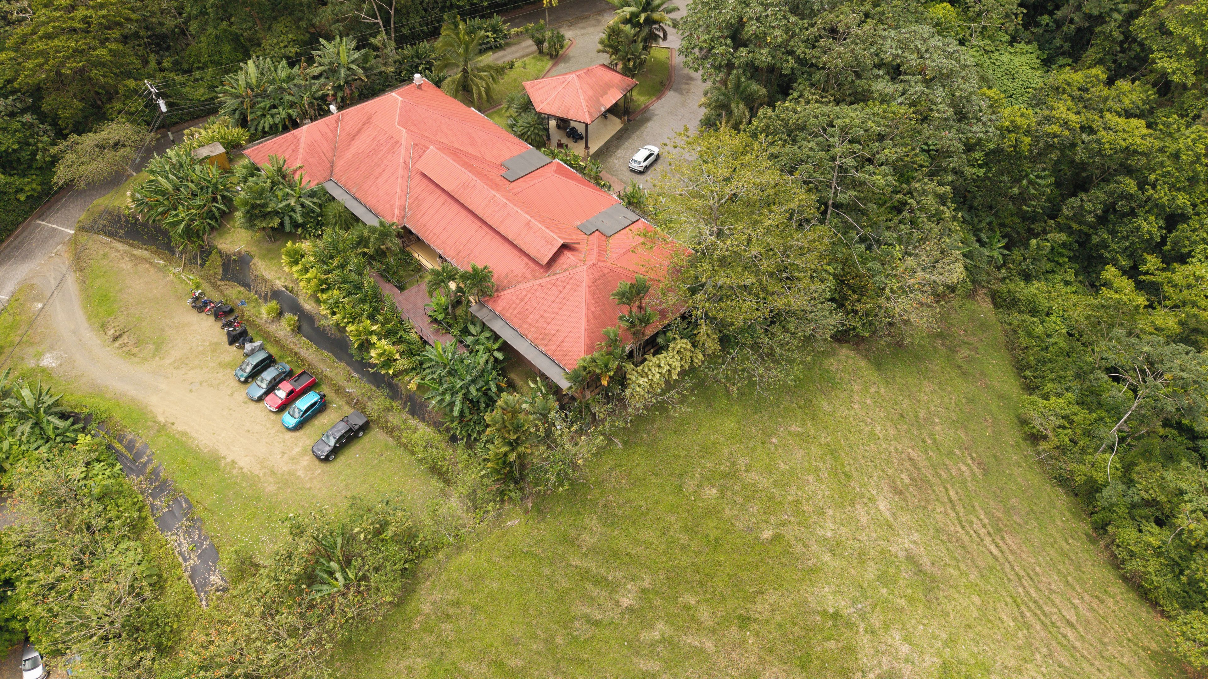 An aerial view of a property with a red-roofed building, a covered outdoor seating area, and a parking lot with several cars.