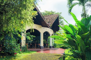 A covered outdoor seating area with tables and chairs, surrounded by lush greenery and a pathway. - Arenal Rainforest (La Fortuna)