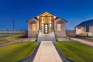 A two-story building with a central entrance, a covered porch, and a driveway leading to the front door. - Arch Ray  Retreat - Luxury Home w/firepit & grill (Fredericksburg)