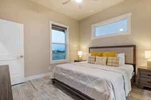 A bedroom with a bed, bedside tables, a window, and a door. - Arch Ray  Retreat - Luxury Home w/firepit & grill (Fredericksburg)