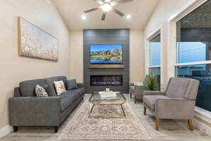 A living room with a flat-screen TV, a fireplace, a sofa, a coffee table, and a chair. - Arch Ray  Retreat - Luxury Home w/firepit & grill (Fredericksburg)