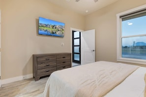 Ein Schlafzimmer mit einem Bett, einer Kommode, einem an der Wand befestigten Fernseher und einem Fenster mit Blick.