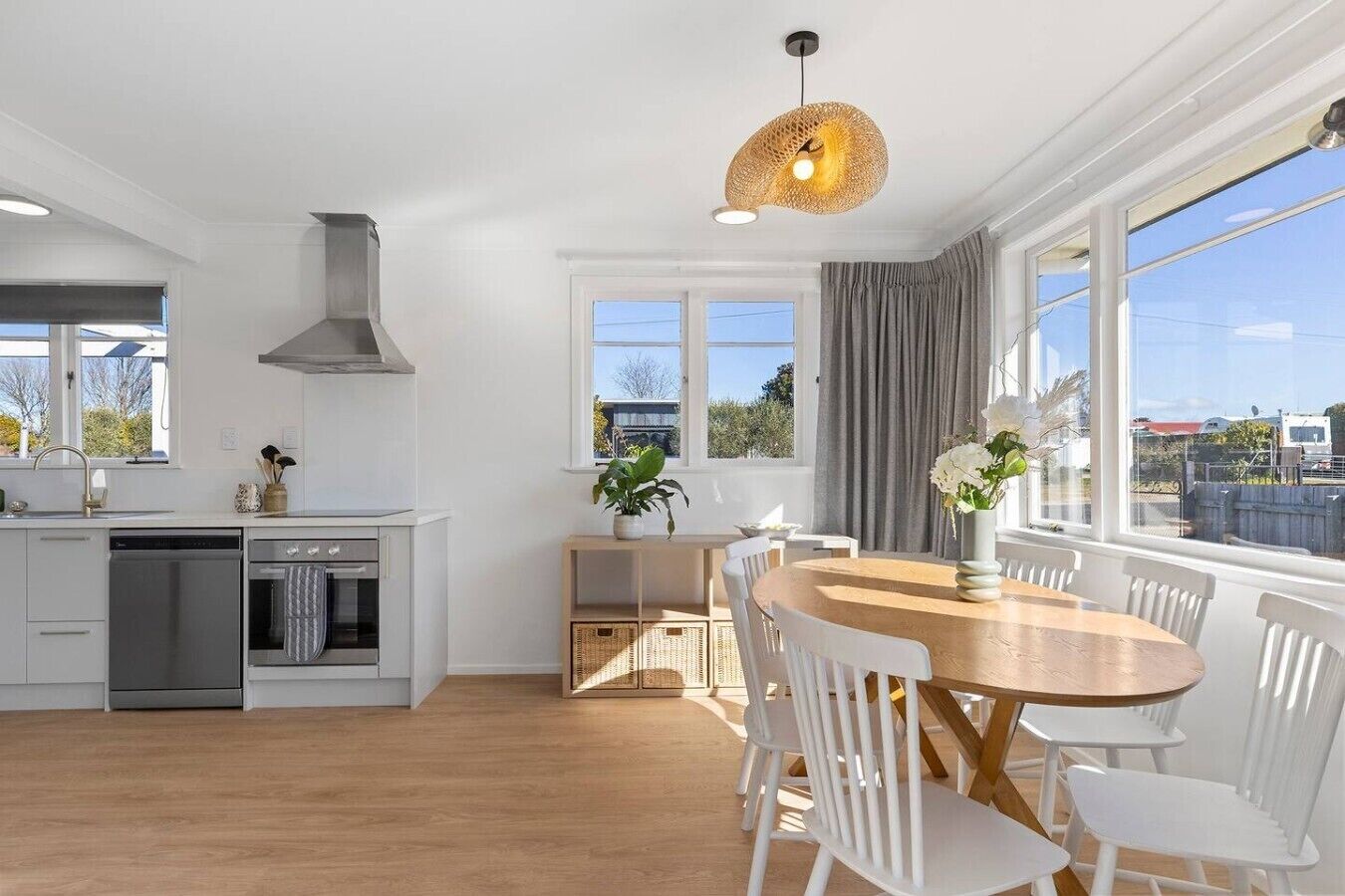 Een moderne keuken met witte kasten, een eethoek met een houten tafel en witte stoelen, en grote ramen met uitzicht.