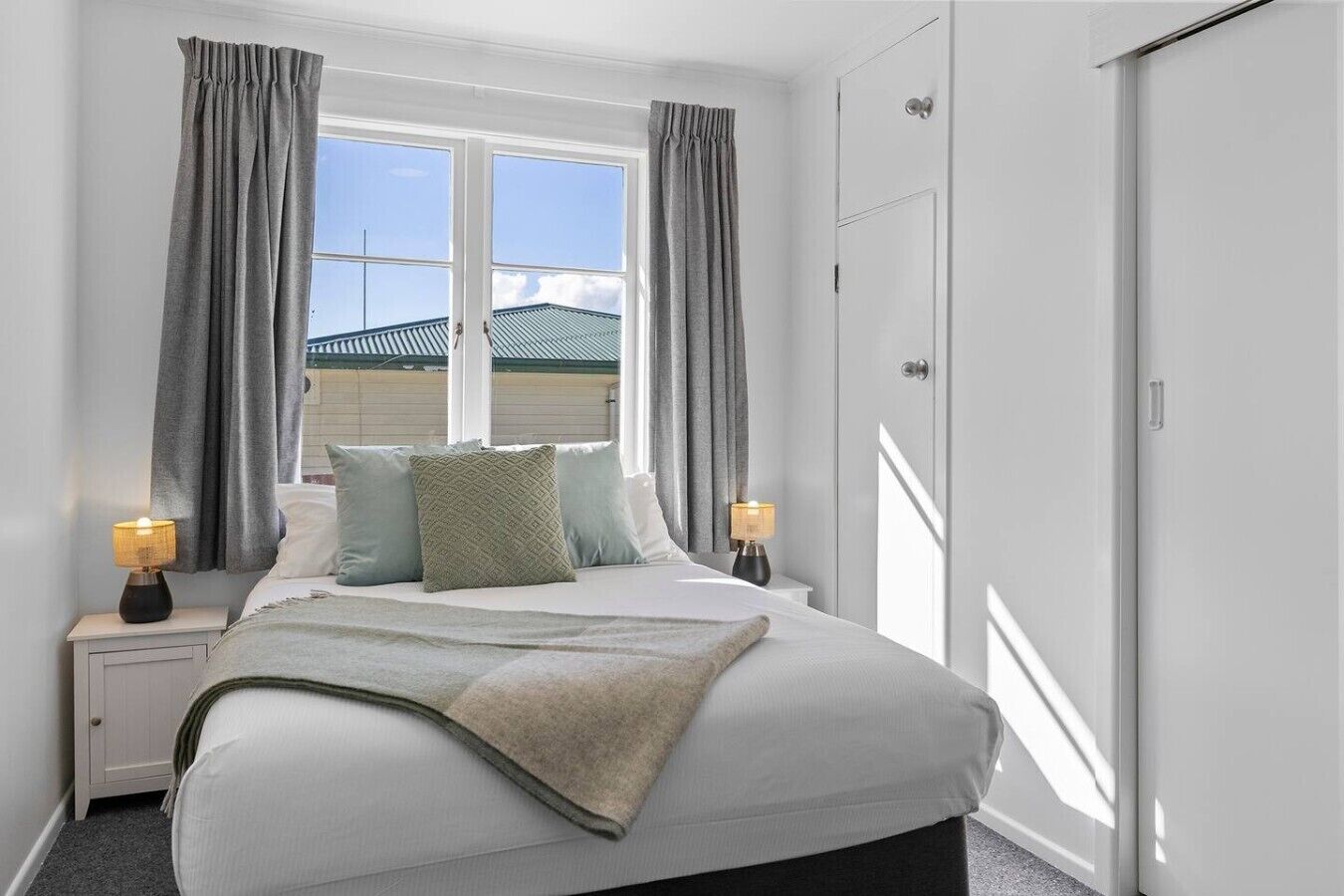Une chambre à coucher avec un lit, deux tables de chevet, une fenêtre avec des rideaux et une armoire.