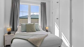 A bedroom with a bed, two bedside tables, a window with curtains, and a wardrobe.