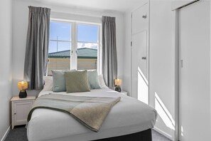 A bedroom with a bed, two bedside tables, a window with curtains, and a wardrobe. - The White Veranda - classic character and modern comfort (Taupō)