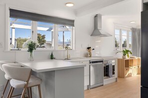 Una cuina moderna amb una illa central, forn integrat i un gran finestral que aporta llum natural.