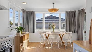 A modern kitchen with white cabinetry, a dining area with a round table and white chairs, and a large window with a view of a mountain.