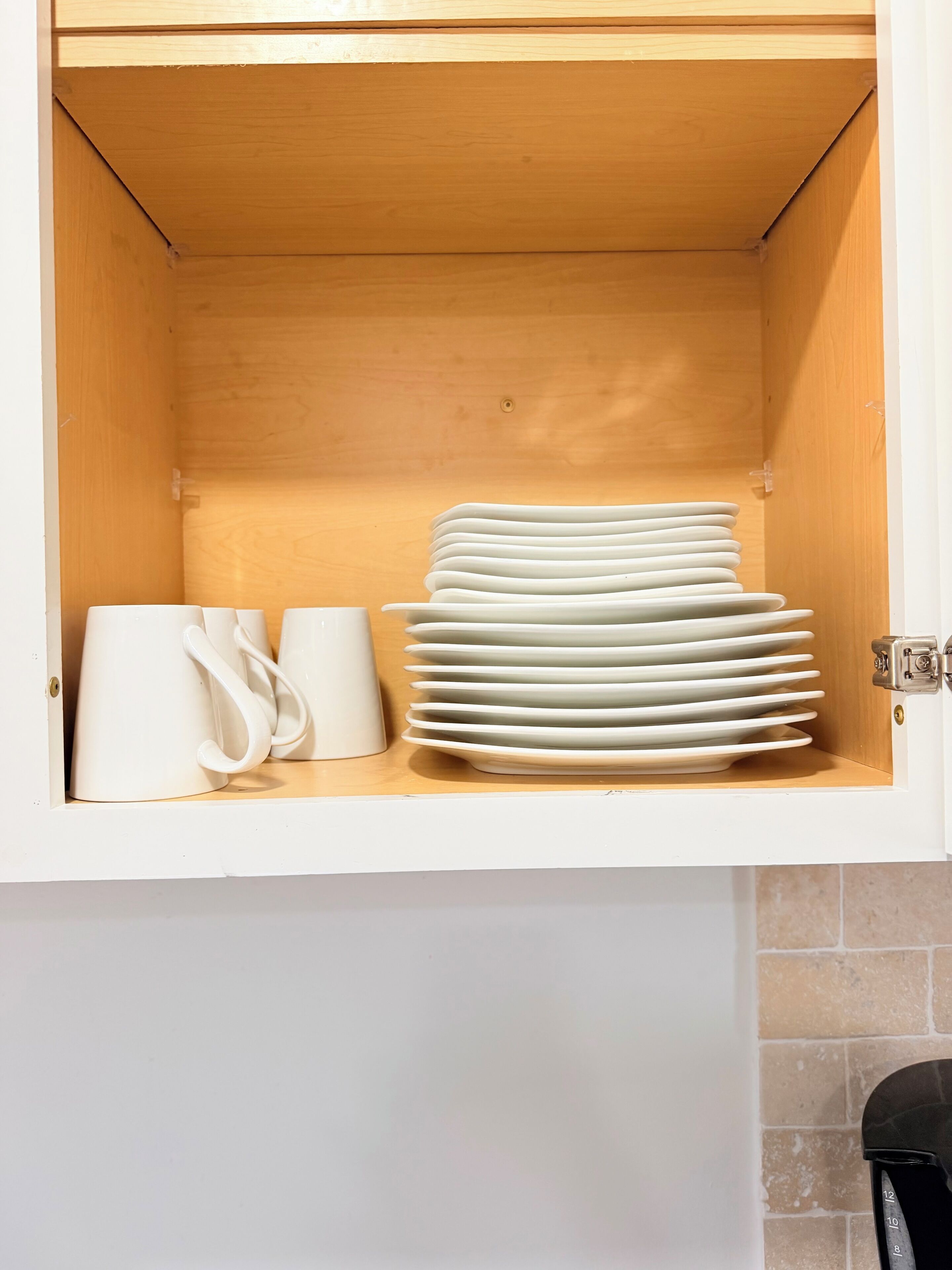 Un meuble de cuisine dont l’intérieur est en bois, contenant des assiettes blanches empilées et un pichet blanc.