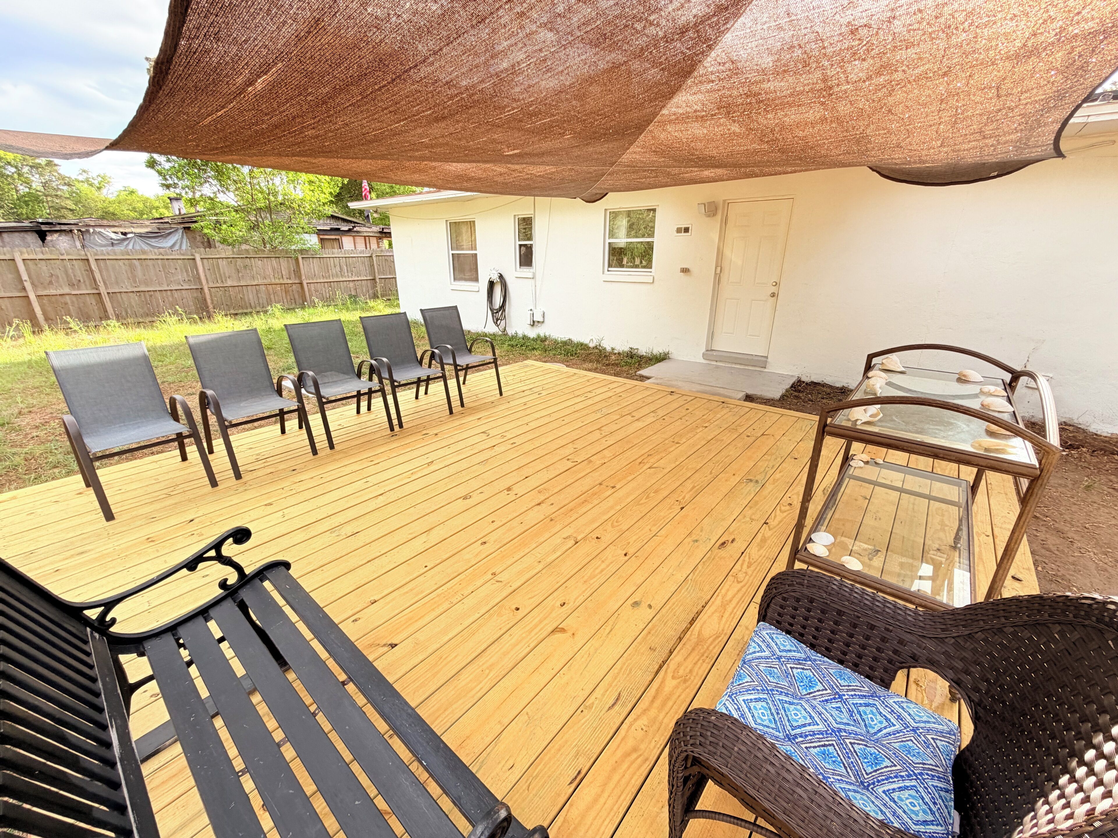 A wooden deck with chairs and a table, a covered area with a roof, and a house in the background.
