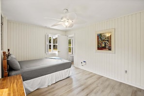 A bedroom with a bed, a ceiling fan, a window, and a painting on the wall. - Litts Go Play-Soundside retreat with 4 bedrooms, deck, and ocean views. (Kitty Hawk)