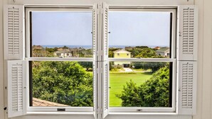 A bay window with four panes, each offering a view of a residential area with houses and greenery. - Litts Go Play-Soundside retreat with 4 bedrooms, deck, and ocean views. (Kitty Hawk)