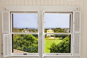 A bay window with four panes, each offering a view of a residential area with houses and greenery. - Litts Go Play-Soundside retreat with 4 bedrooms, deck, and ocean views. (Kitty Hawk)