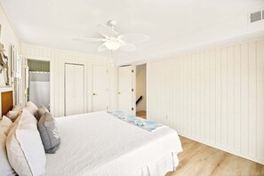 Une chambre à coucher avec un lit, un ventilateur de plafond et une vue sur un escalier.