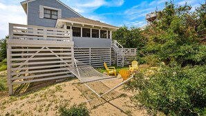 A house with a covered porch, a wooden deck, and a sandy area with chairs. - Litts Go Play-Soundside retreat with 4 bedrooms, deck, and ocean views. (Kitty Hawk)
