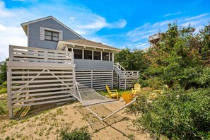 A house with a covered porch, a wooden deck, and a sandy area with chairs. - Litts Go Play-Soundside retreat with 4 bedrooms, deck, and ocean views. (Kitty Hawk)