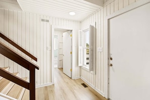A hallway with white paneled walls, a wooden staircase, and a closed door. - Litts Go Play-Soundside retreat with 4 bedrooms, deck, and ocean views. (Kitty Hawk)