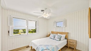 A bedroom with a bed, nightstands, a ceiling fan, and two windows with shutters. - Litts Go Play-Soundside retreat with 4 bedrooms, deck, and ocean views. (Kitty Hawk)