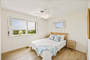 A bedroom with a bed, nightstands, a ceiling fan, and two windows with shutters. - Litts Go Play-Soundside retreat with 4 bedrooms, deck, and ocean views. (Kitty Hawk)