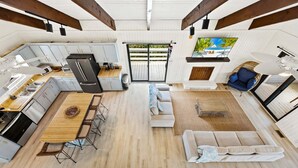 A spacious open-plan living area with a kitchen, dining table, sofa, and a large window with a view. - Litts Go Play-Soundside retreat with 4 bedrooms, deck, and ocean views. (Kitty Hawk)