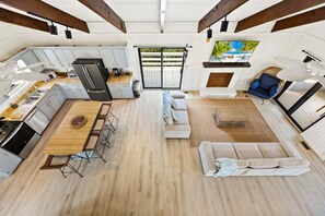 A spacious open-plan living area with a kitchen, dining table, sofa, and a large window with a view. - Litts Go Play-Soundside retreat with 4 bedrooms, deck, and ocean views. (Kitty Hawk)