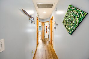 A hallway with a wooden floor, a ceiling vent, a wall-mounted artwork, and a door leading to another room. - Till Next Time - hot tub, tiki bar, EV charger, and beach access. (Kill Devil Hills)
