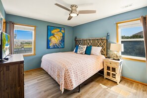 A bedroom with a bed, a ceiling fan, a painting, a nightstand, and a window. - Till Next Time - hot tub, tiki bar, EV charger, and beach access. (Kill Devil Hills)
