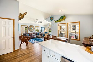 A spacious living area with a leather sofa, wooden coffee table, and a dining table with chairs. - Till Next Time - hot tub, tiki bar, EV charger, and beach access. (Kill Devil Hills)
