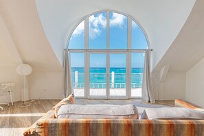 Quarto com uma grande janela em arco que dá para uma varanda com vista para o mar.