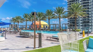 A poolside area with lounge chairs, palm trees, and a view of the ocean. - Oceanview Highrise - Amenities- 6 people (Hollywood)
