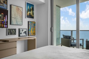 A modern bedroom with a large bed, a desk, and a balcony with a view of the sky and clouds. - LYFE Resort | 24th Floor Ocean View + Balcony (Hollywood)