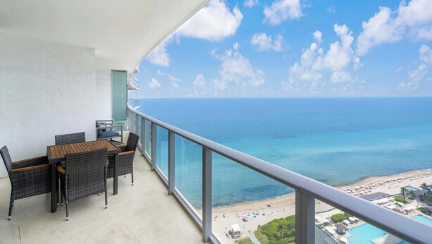A balcony with a table and chairs, overlooking a beach and the ocean. - Oceanview Highrise - Amenities- 6 people (Hollywood)