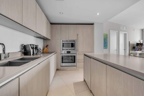 A modern kitchen with stainless steel appliances, a central island, and light wood cabinetry. - LYFE Resort | 24th Floor Ocean View + Balcony (Hollywood)