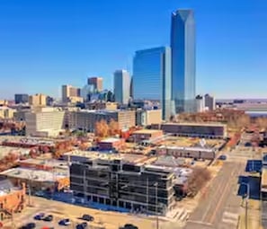 A cityscape with modern buildings, including a prominent skyscraper, and a construction site with visible scaffolding. - TB Signature Lofts – Unit 210 in Downtown OKC (Oklahoma City)