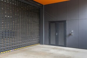 A closed garage door with a metal mesh pattern, a grey wall, and a concrete floor. - Heart of CBD - Walk to ONE NZ Stadium + Parking (Christchurch)