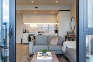 A modern living space with a grey sofa, a coffee table with a plant, and a kitchen in the background. - Heart of CBD - Walk to ONE NZ Stadium + Parking (Christchurch)