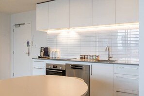 A modern kitchen with white cabinetry, a built-in oven, a dishwasher, and a coffee maker. - Heart of CBD - Walk to ONE NZ Stadium + Parking (Christchurch)