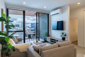 A modern living room with a sofa, a coffee table, and a TV mounted on the wall. - Heart of CBD - Walk to ONE NZ Stadium + Parking (Christchurch)