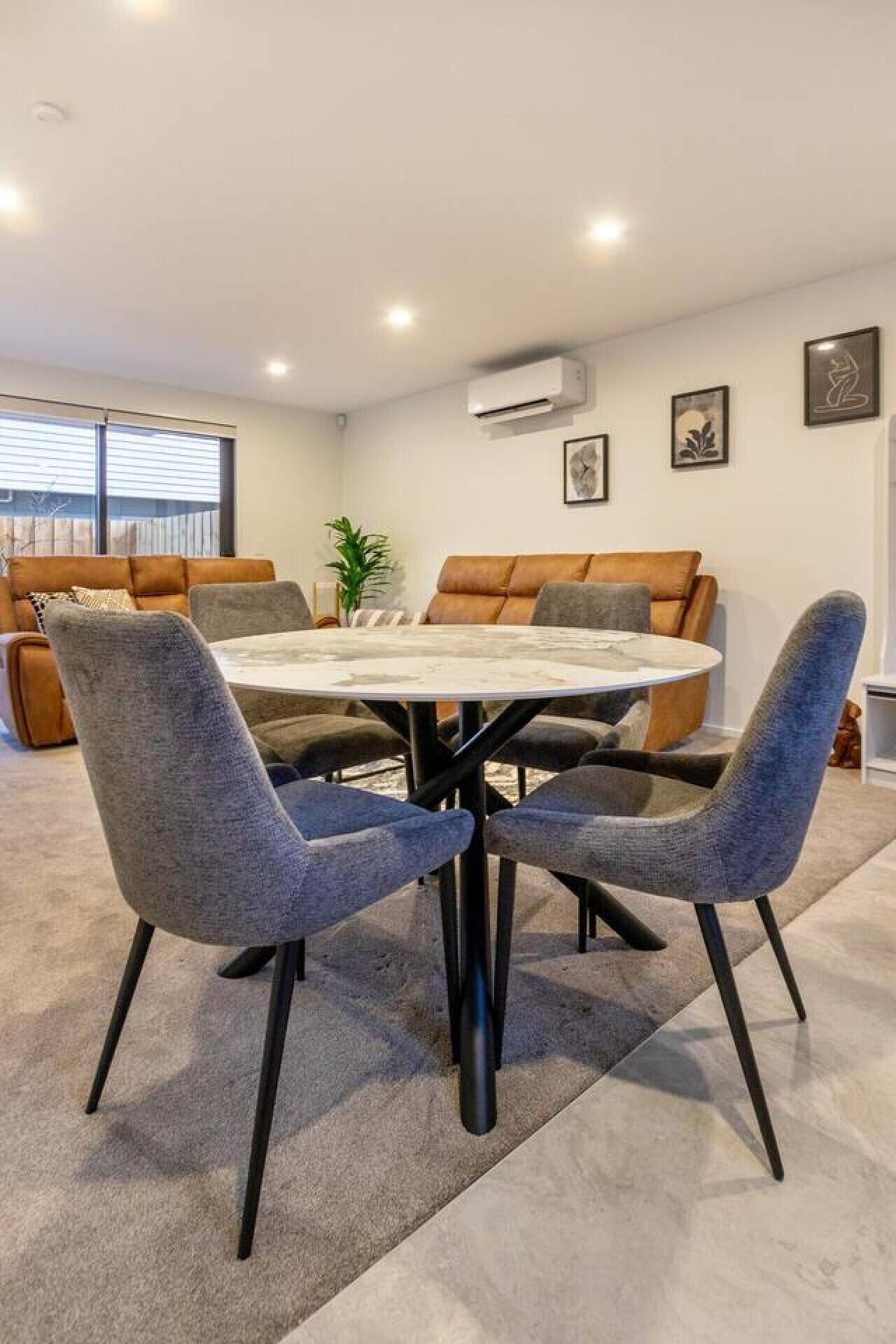 A modern living room with a round table and four chairs, a sofa, and a potted plant.