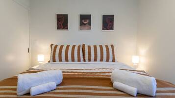 A hotel room with a bed, striped bedding, two pillows, two bedside lamps, and three framed pictures on the wall.