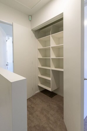 A walk-in closet with multiple shelves and a carpeted floor. - Ultimate City Comfort - Carpark + EV (Christchurch)