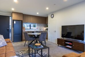 A modern living space with a dining area, a kitchen, a television, and a sofa. - Ultimate City Comfort - Carpark + EV (Christchurch)