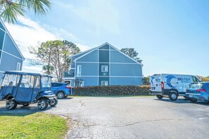 A large building with a blue exterior, a parking lot with several vehicles, and a hedge in front. - Deerfield at Golf Colony Unit 11R with Pool Access (Surfside Beach)