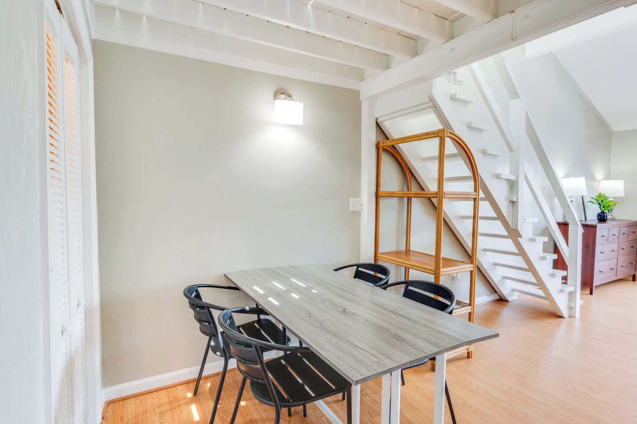 A dining area with a table and chairs, a staircase, and a wall-mounted light fixture.