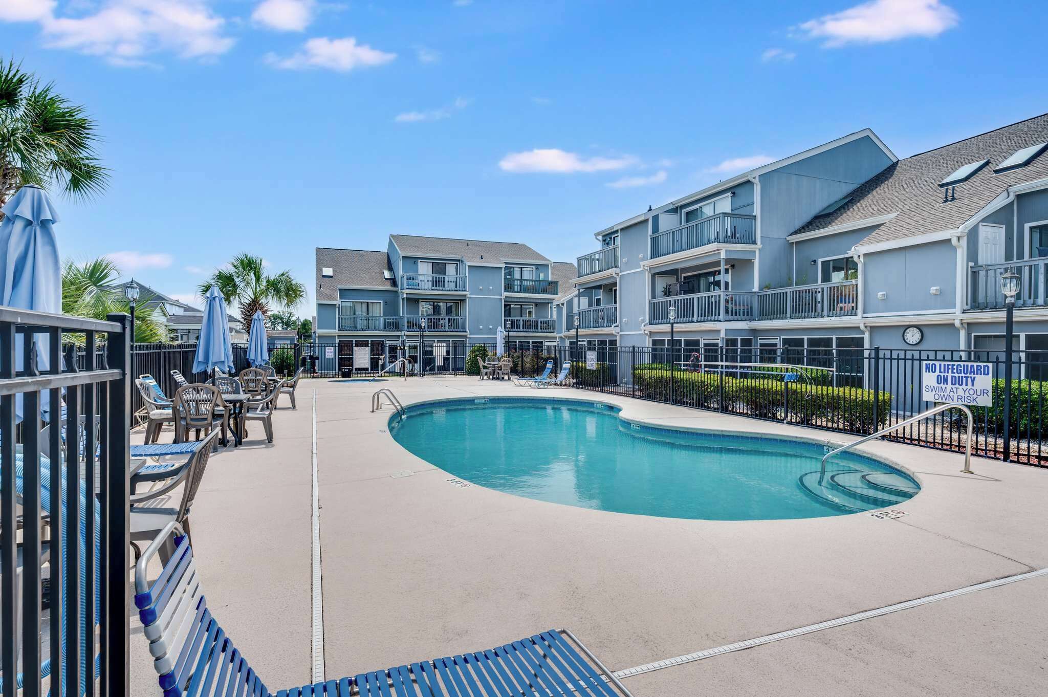 A swimming pool area with lounge chairs and umbrellas, surrounded by multi-story residential buildings.