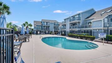 A swimming pool area with lounge chairs and umbrellas, surrounded by multi-story residential buildings.