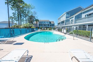 A swimming pool with lounge chairs, a blue fence, and a building with multiple balconies in the background. - Deerfield at Golf Colony Unit 11R with Pool Access (Surfside Beach)