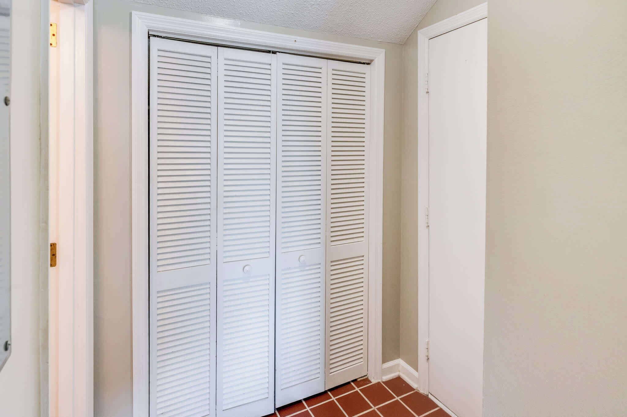 A closed white closet with horizontal louvered doors and a white door to the right.