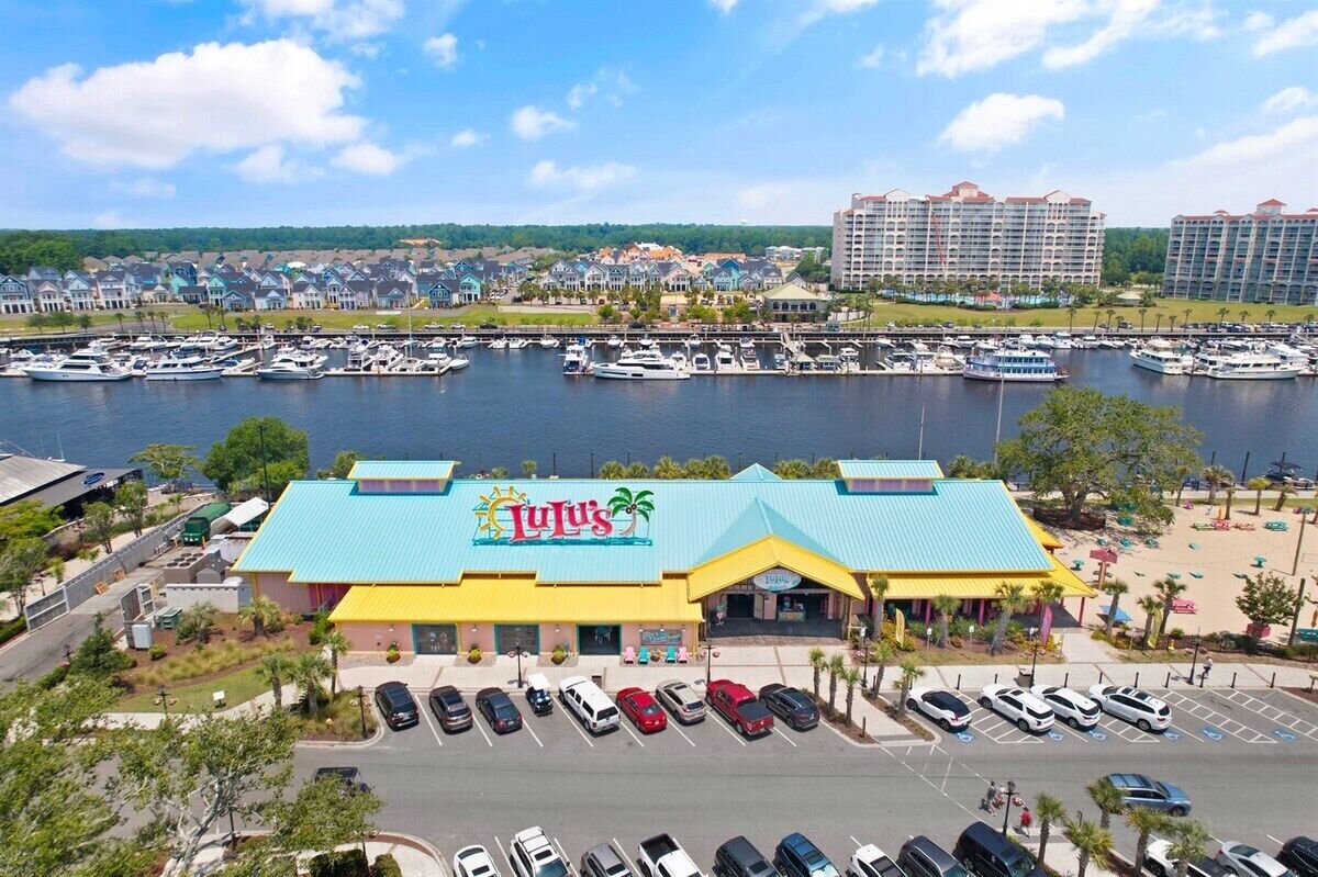 Uma marina com barcos, um estacionamento e um edifício com telhado azul e uma placa com o nome 'Lulu's'.